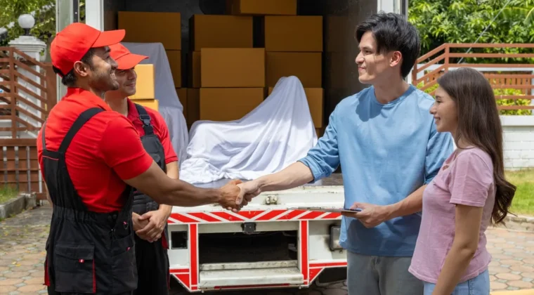Two removalists shaking hands with a couple beside a loaded moving truck