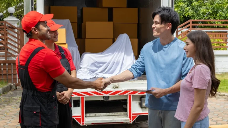 Two removalists shaking hands with a couple beside a loaded moving truck